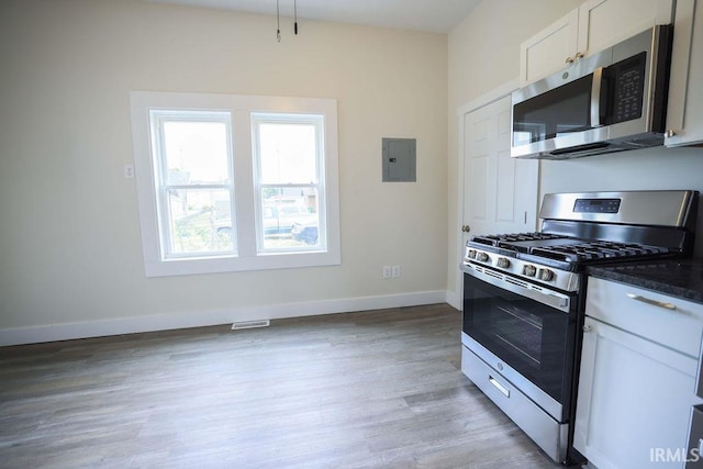 kitchen featuring light wood-type flooring, dark stone counters, white cabinetry, electric panel, and appliances with stainless steel finishes