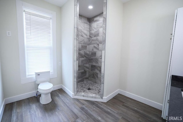 bathroom with hardwood / wood-style floors, toilet, and a tile shower