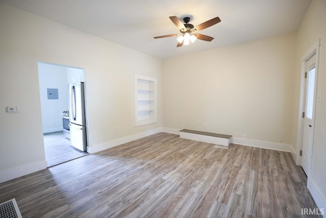 spare room with hardwood / wood-style floors, ceiling fan, electric panel, and built in shelves