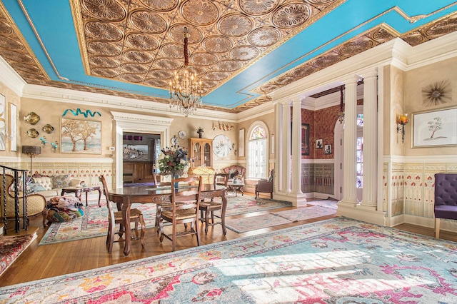 dining room with ornamental molding, wood-type flooring, ornate columns, and a chandelier