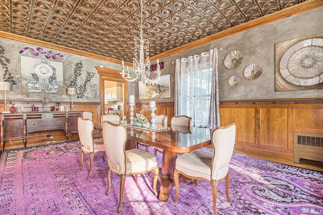 dining area with wood walls, ornamental molding, an inviting chandelier, and radiator heating unit