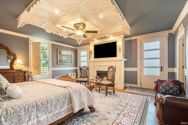 bedroom featuring crown molding, a premium fireplace, hardwood / wood-style flooring, and ceiling fan