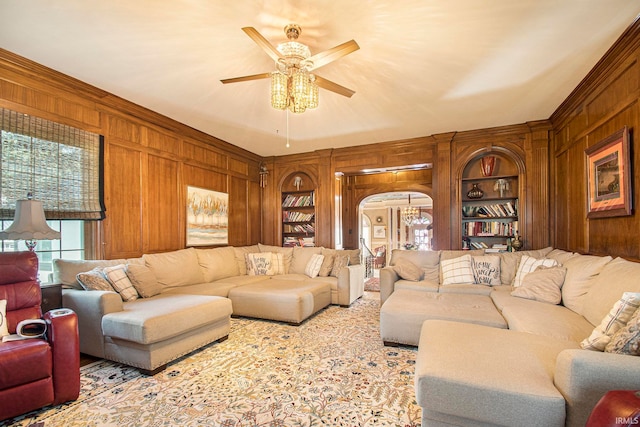 living room featuring built in shelves, ceiling fan, ornamental molding, and wooden walls