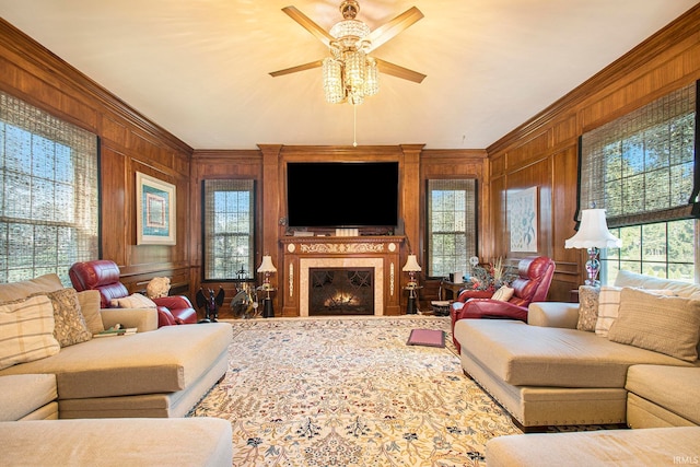 living room featuring ceiling fan, wooden walls, crown molding, and a healthy amount of sunlight