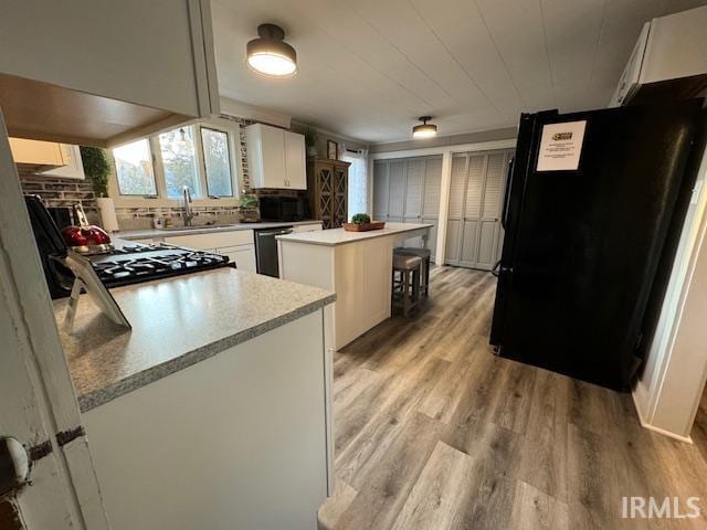 kitchen featuring a kitchen island, black appliances, a stone fireplace, light wood-type flooring, and white cabinets