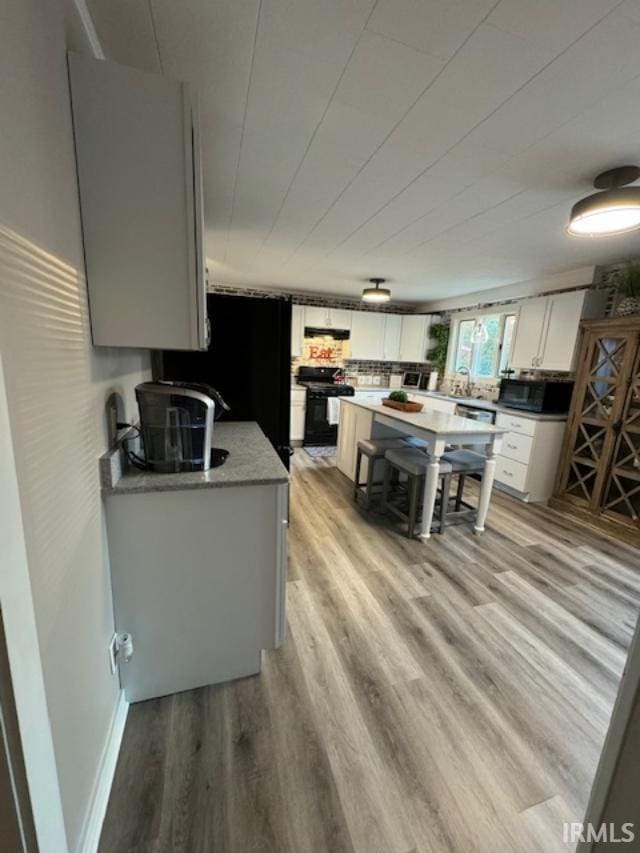 kitchen with light wood-type flooring, white cabinets, and black appliances