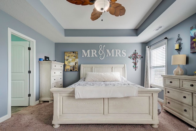 bedroom with light carpet, a tray ceiling, and ceiling fan