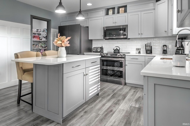 kitchen featuring appliances with stainless steel finishes, a center island, a breakfast bar area, decorative light fixtures, and light hardwood / wood-style flooring