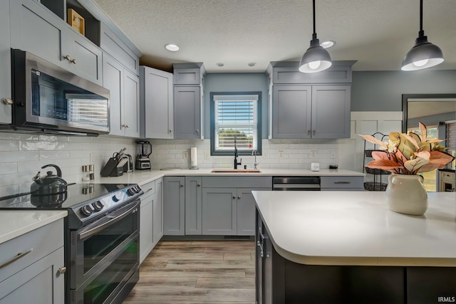 kitchen with decorative backsplash, appliances with stainless steel finishes, pendant lighting, gray cabinets, and sink