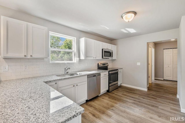 kitchen with sink, white cabinetry, backsplash, stainless steel appliances, and light stone countertops