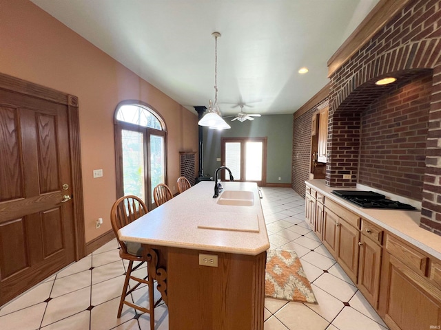 kitchen with black gas stovetop, sink, light tile patterned flooring, pendant lighting, and a center island with sink