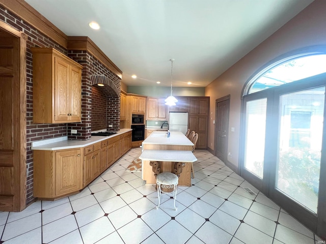 kitchen with decorative light fixtures, brick wall, black appliances, light tile patterned flooring, and a center island with sink