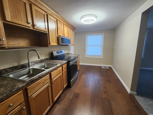 kitchen featuring stainless steel appliances, backsplash, dark hardwood / wood-style floors, dark stone countertops, and sink