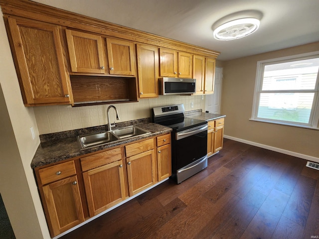 kitchen featuring backsplash, dark hardwood / wood-style floors, sink, appliances with stainless steel finishes, and dark stone counters