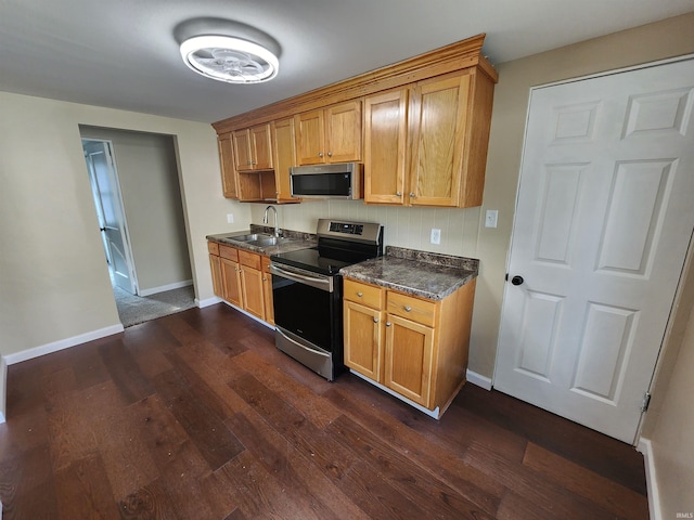 kitchen featuring appliances with stainless steel finishes, dark stone countertops, dark hardwood / wood-style floors, and sink