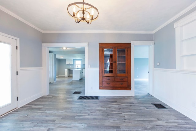 unfurnished dining area with hardwood / wood-style floors, ornamental molding, and an inviting chandelier