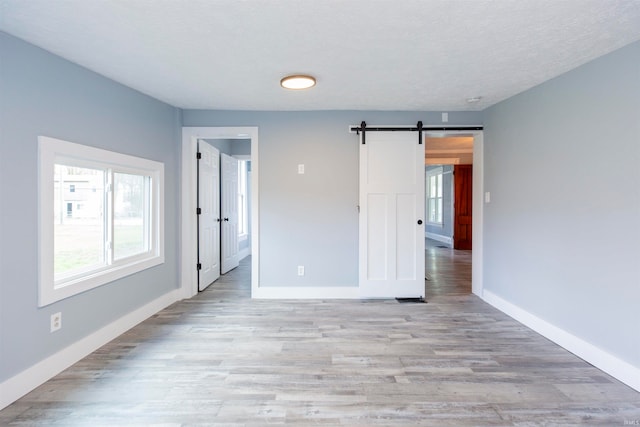 unfurnished room featuring a barn door, light hardwood / wood-style floors, and a textured ceiling