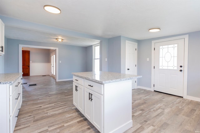 kitchen with white cabinets, light wood-type flooring, a kitchen island, and light stone counters