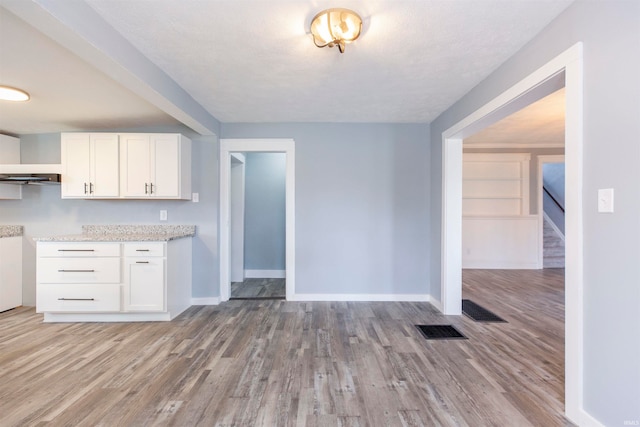 kitchen with white cabinets, a textured ceiling, light wood-type flooring, and ventilation hood