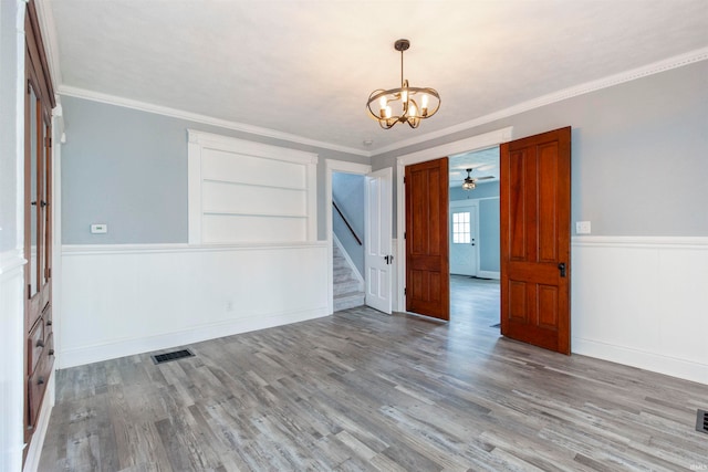 spare room with built in features, light hardwood / wood-style floors, ceiling fan with notable chandelier, and ornamental molding