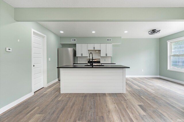 3615 Lindbergh Blvd, Fort Wayne, IN 46806 - kitchen featuring dark countertops, a sink, a kitchen island with sink, light wood-style floors, and white cabinetry