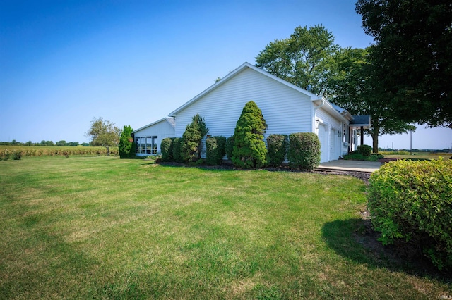 view of side of property with a lawn, a rural view, and a garage