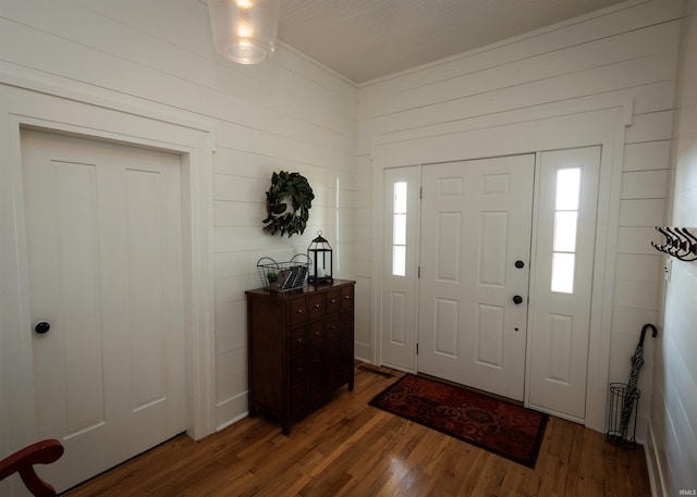 entrance foyer with dark wood-type flooring, wooden walls, and ornamental molding