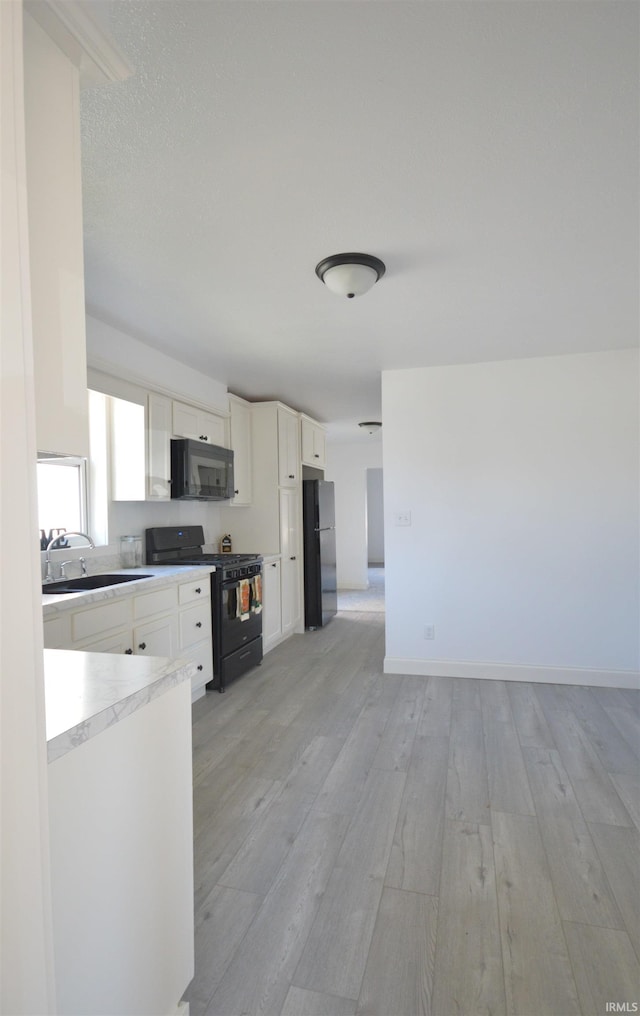 kitchen with light wood-type flooring, black appliances, sink, and white cabinets