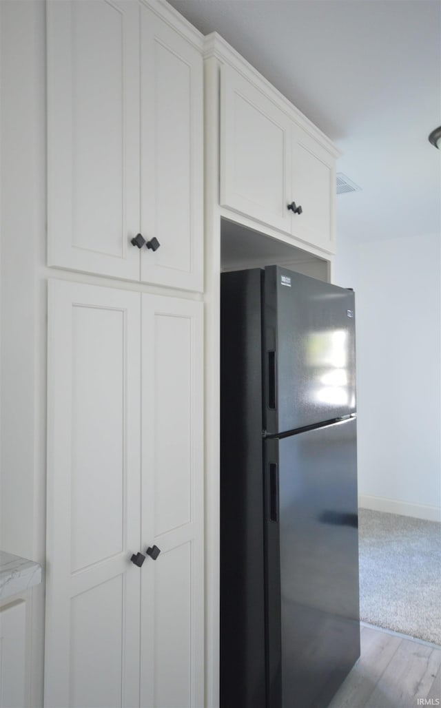 kitchen with light stone counters, hardwood / wood-style floors, stainless steel refrigerator, and white cabinets