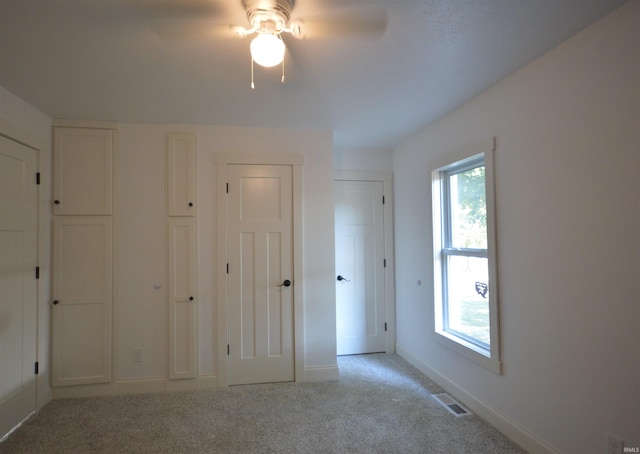 unfurnished bedroom featuring multiple windows, light colored carpet, and ceiling fan