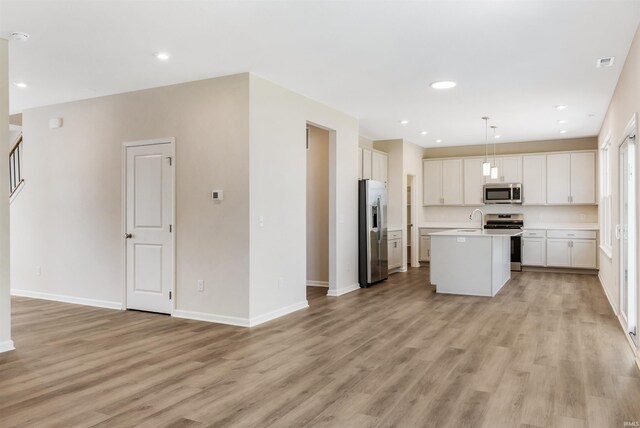 kitchen with light wood-type flooring, appliances with stainless steel finishes, pendant lighting, and an island with sink