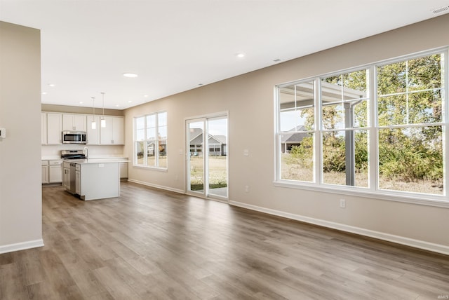 interior space with stainless steel appliances, decorative light fixtures, white cabinets, and light hardwood / wood-style floors