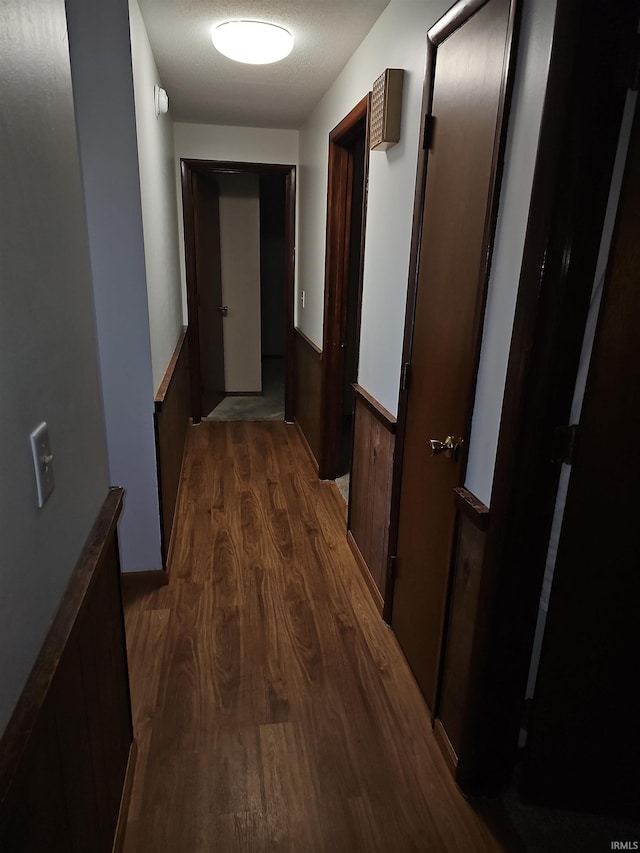 hall featuring a textured ceiling, dark wood-type flooring, and wooden walls