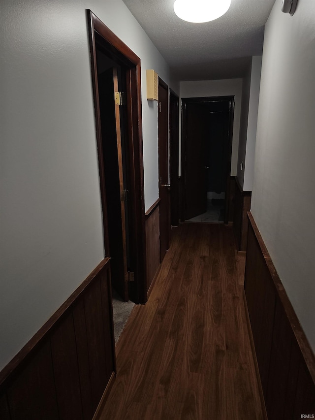 hall with a textured ceiling, dark wood-type flooring, and wooden walls