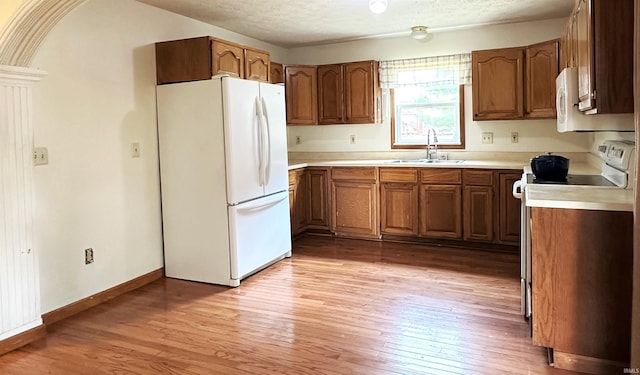 kitchen featuring a textured ceiling, white appliances, sink, and light hardwood / wood-style flooring