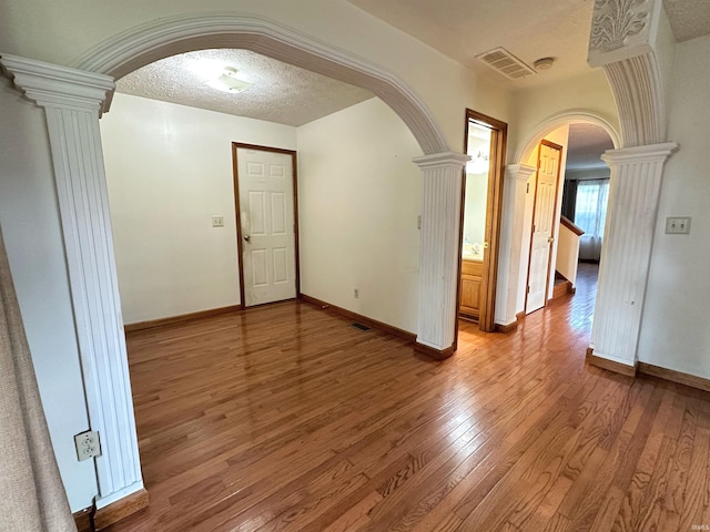 empty room featuring decorative columns, hardwood / wood-style floors, and a textured ceiling