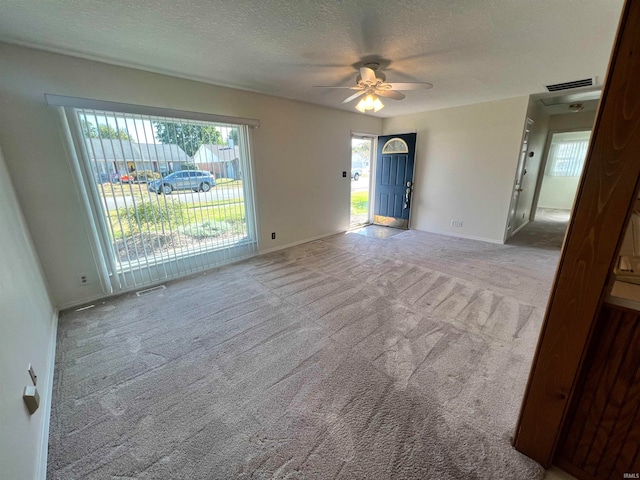 carpeted spare room with a textured ceiling, plenty of natural light, and ceiling fan