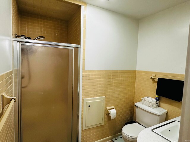 bathroom featuring sink, a shower with door, toilet, and tile walls