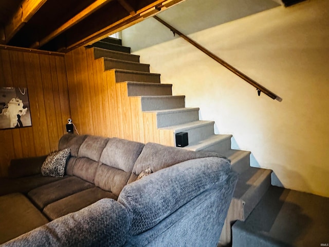 stairway with carpet floors, beamed ceiling, and wooden walls