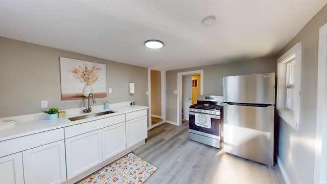 kitchen featuring light wood-type flooring, sink, appliances with stainless steel finishes, and white cabinetry