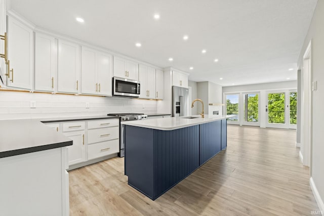 kitchen with white cabinets, sink, a kitchen island with sink, appliances with stainless steel finishes, and light hardwood / wood-style floors