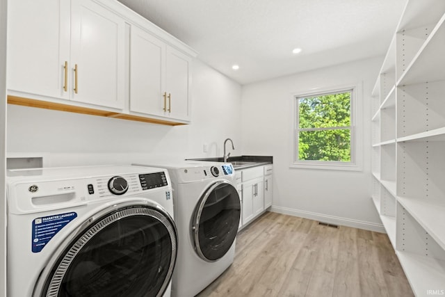 clothes washing area featuring washer and clothes dryer, cabinets, light hardwood / wood-style flooring, and sink