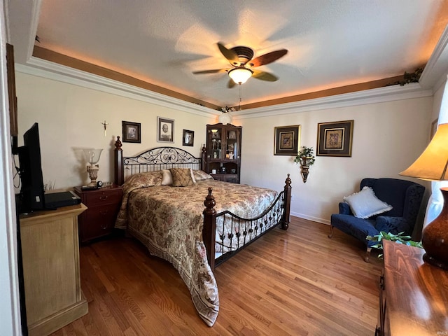 bedroom featuring a textured ceiling, a raised ceiling, hardwood / wood-style floors, ornamental molding, and ceiling fan