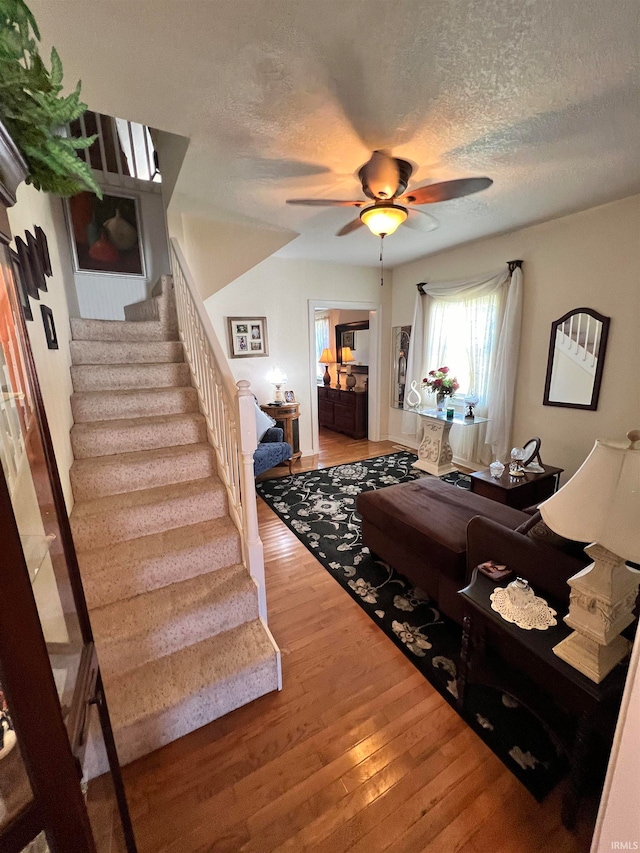 living room featuring ceiling fan, hardwood / wood-style flooring, and a textured ceiling