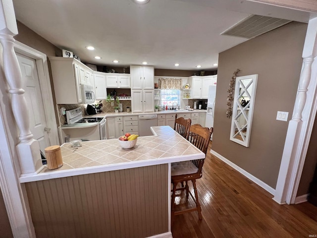 kitchen with white cabinets, white appliances, tile countertops, dark hardwood / wood-style floors, and a breakfast bar