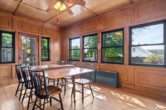 dining area featuring radiator heating unit, light hardwood / wood-style floors, wood walls, ornamental molding, and ceiling fan