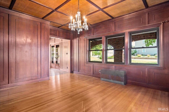 spare room with an inviting chandelier, light wood-type flooring, radiator heating unit, and a healthy amount of sunlight