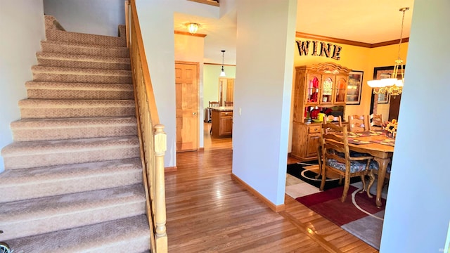 stairs with a chandelier, hardwood / wood-style floors, and crown molding