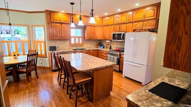 kitchen with appliances with stainless steel finishes, a kitchen island, light hardwood / wood-style flooring, sink, and a notable chandelier