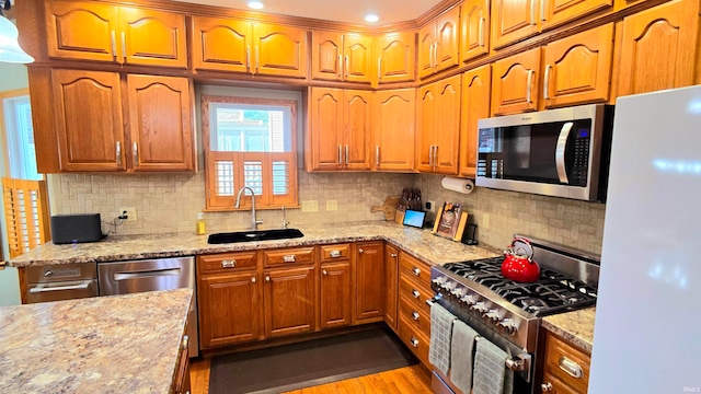 kitchen with light stone countertops, stainless steel appliances, light wood-type flooring, and sink